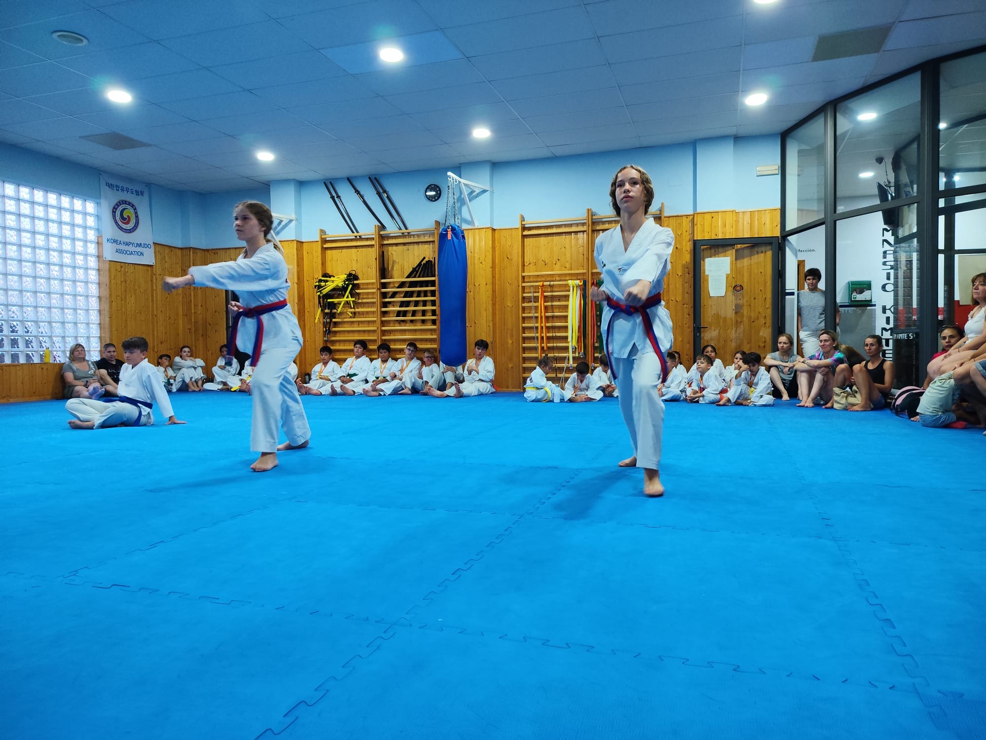 Dos deportistas practican poomsae en el tatami de Kimte’s mientras el grupo observa